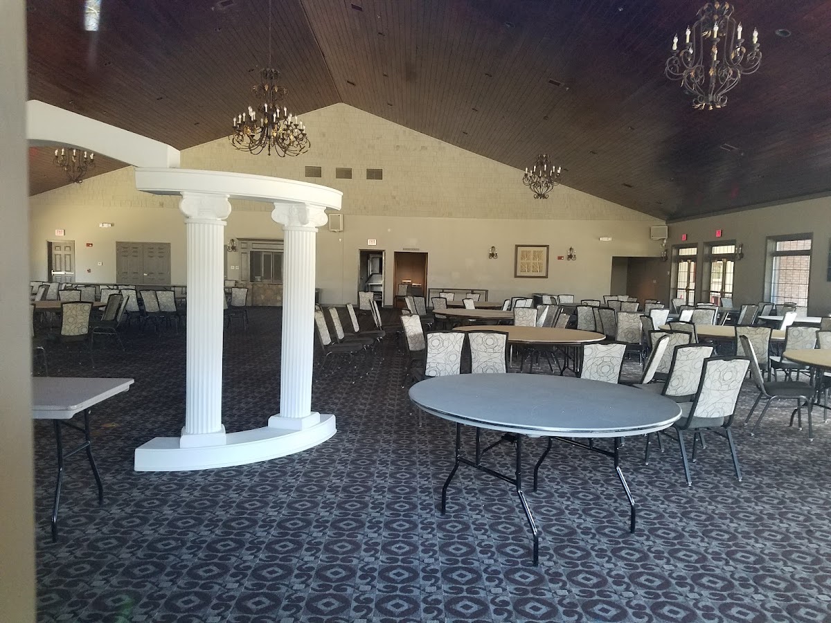 Spacious banquet hall with round tables, white columns, and chandeliers under a vaulted ceiling
