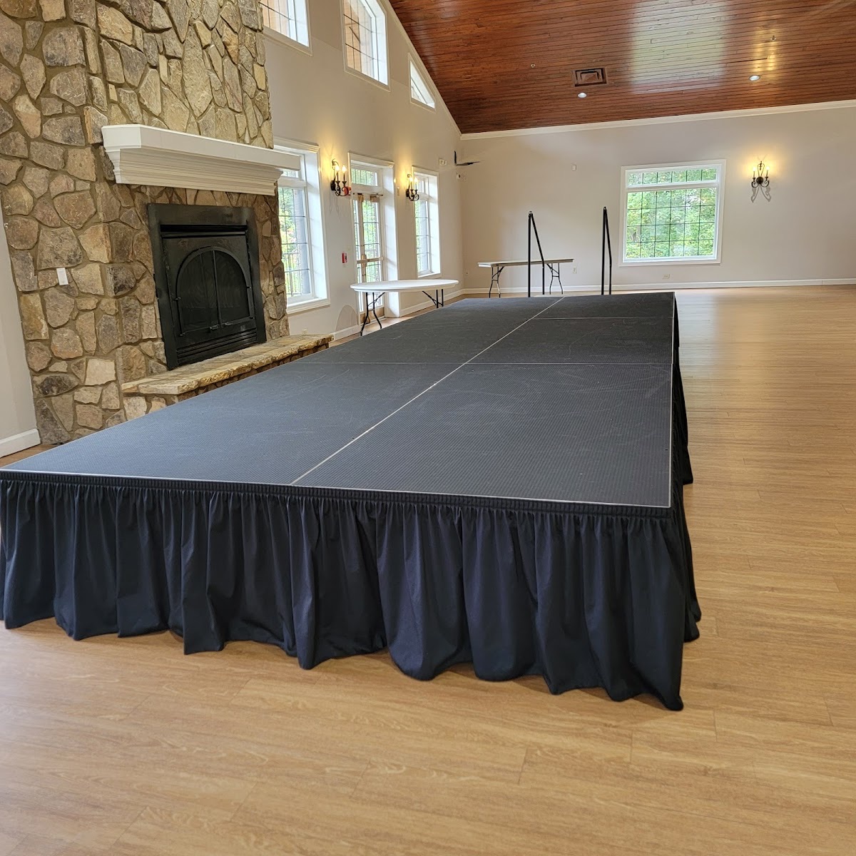 Open event hall with a stage, stone fireplace, and soaring wood-beamed ceiling