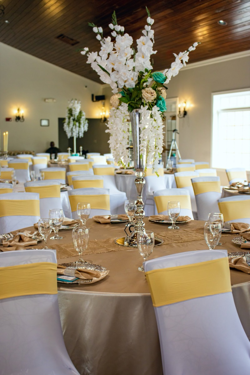 Banquet table detail with gold linens, place settings, and a tall white floral centerpiece